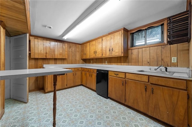kitchen featuring brown cabinetry, dishwasher, a sink, light countertops, and wooden walls