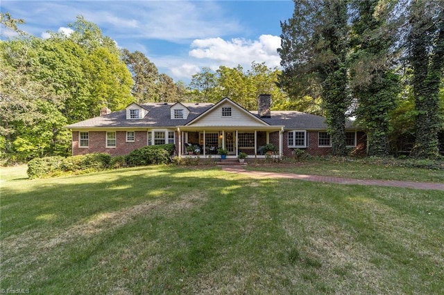 view of front facade featuring covered porch, brick siding, a chimney, and a front yard