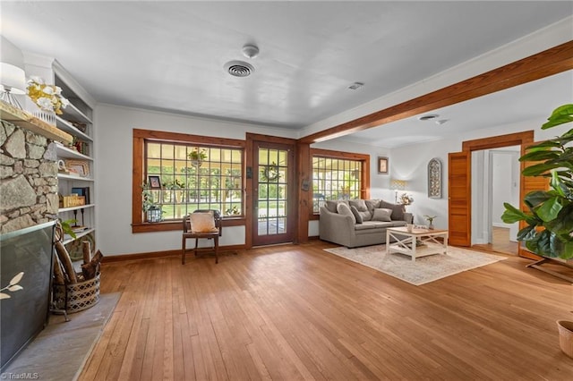 living room featuring visible vents, beam ceiling, a fireplace, baseboards, and light wood-type flooring