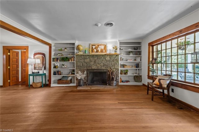 living area featuring visible vents, a fireplace, built in shelves, wood finished floors, and baseboards