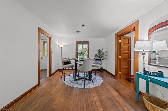 dining space featuring wood-type flooring, baseboards, and crown molding