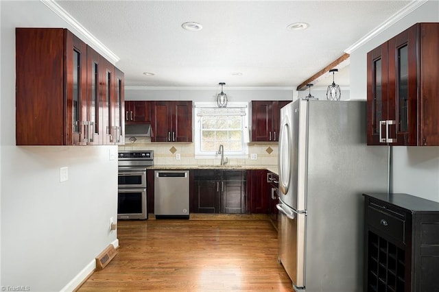 kitchen featuring appliances with stainless steel finishes, a sink, crown molding, light wood-style flooring, and backsplash