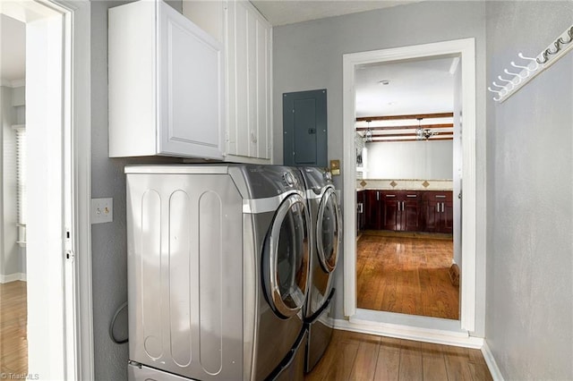 clothes washing area with electric panel, wood finished floors, washer and clothes dryer, cabinet space, and baseboards