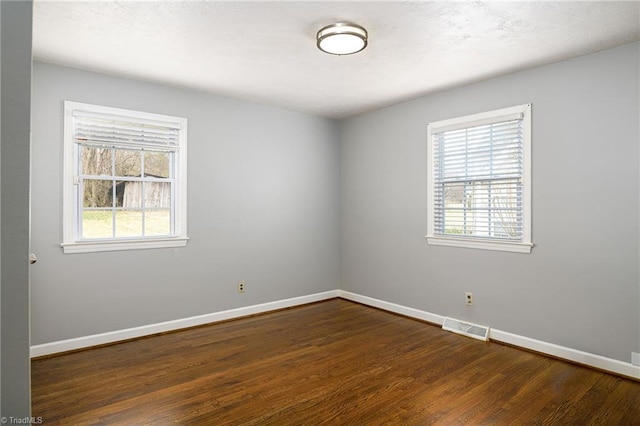unfurnished room featuring plenty of natural light, dark wood finished floors, and baseboards