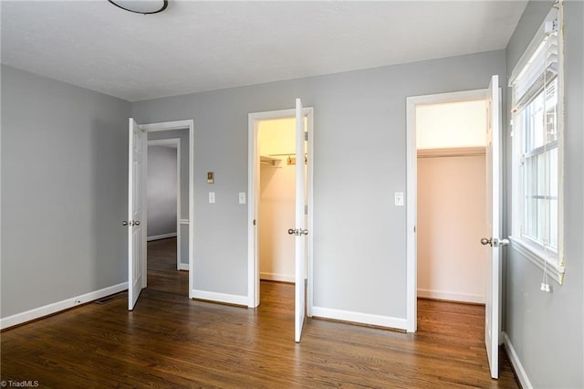 unfurnished bedroom with a spacious closet, wood finished floors, baseboards, and a closet