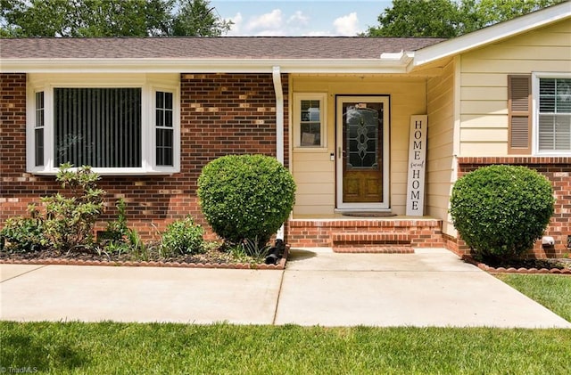 doorway to property with brick siding and roof with shingles