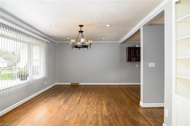 spare room featuring a chandelier, dark wood finished floors, ornamental molding, baseboards, and a textured ceiling