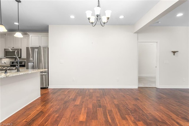 kitchen featuring light stone counters, dark wood-style floors, recessed lighting, an inviting chandelier, and appliances with stainless steel finishes