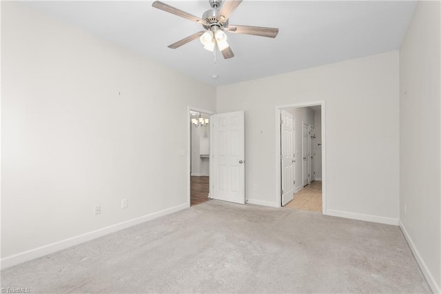 unfurnished bedroom featuring baseboards, ceiling fan with notable chandelier, and light colored carpet