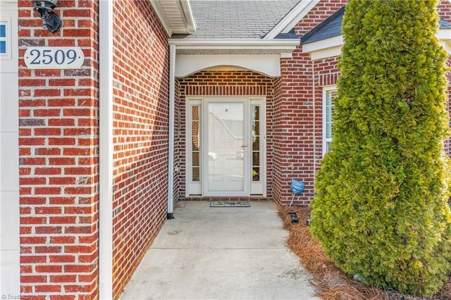 doorway to property with a shingled roof and brick siding