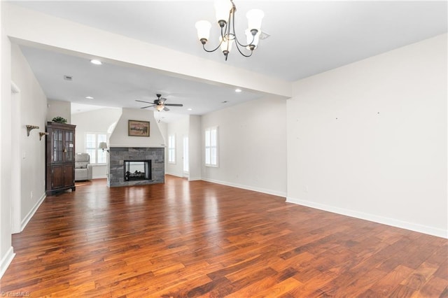 unfurnished living room featuring dark wood-type flooring, a stone fireplace, baseboards, and ceiling fan with notable chandelier