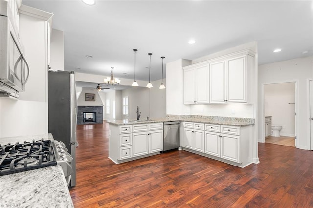 kitchen with appliances with stainless steel finishes, open floor plan, white cabinetry, a stone fireplace, and a peninsula