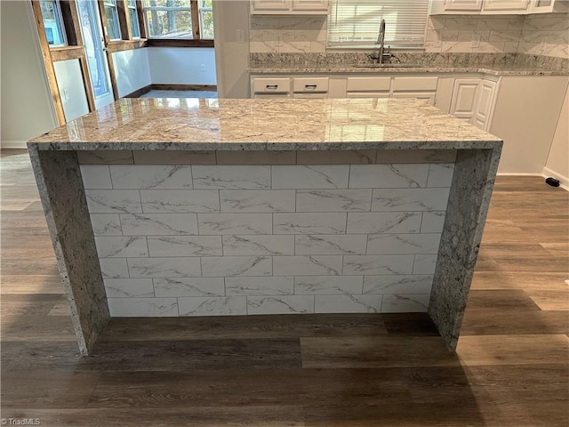 interior details featuring wood-type flooring, light stone countertops, white cabinets, and decorative backsplash