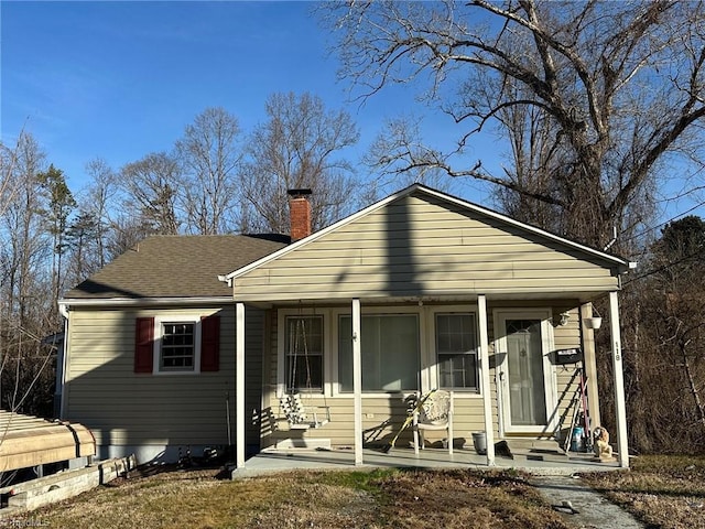 view of front of house featuring a porch, a shingled roof, and a chimney