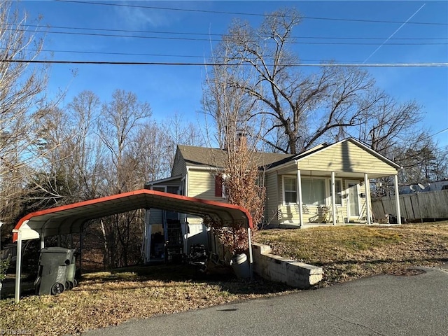 view of front of property featuring covered porch, a carport, a chimney, and fence