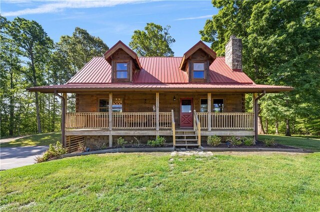 view of front of home featuring covered porch, a chimney, a front lawn, and metal roof