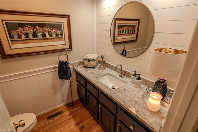 bathroom featuring visible vents, a wainscoted wall, toilet, wood finished floors, and vanity