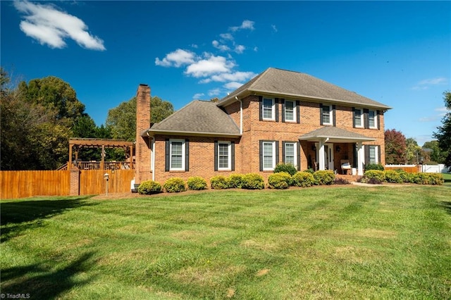 colonial house with a front yard, fence, a pergola, and a chimney