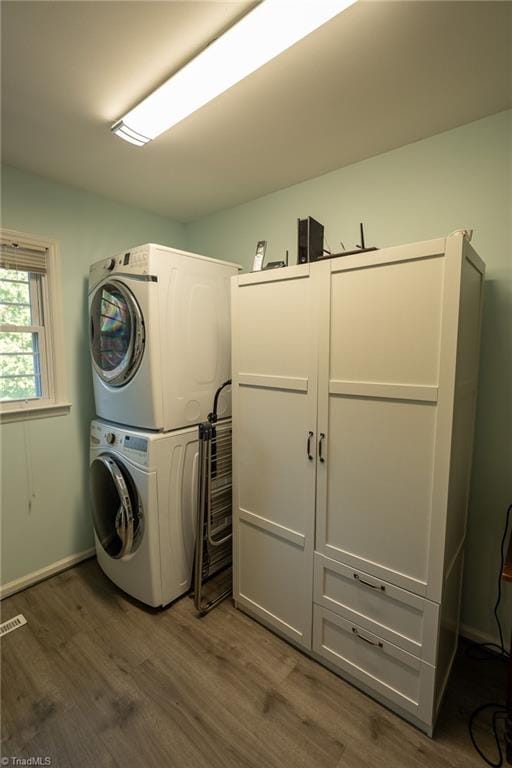 laundry area with laundry area, wood finished floors, stacked washer and clothes dryer, and baseboards