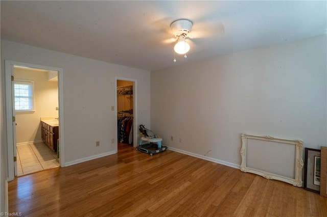 unfurnished bedroom with baseboards, a spacious closet, light wood-style floors, a closet, and connected bathroom