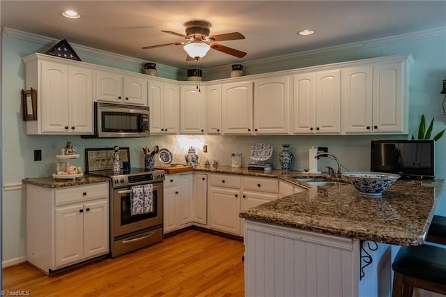 kitchen featuring a sink, a kitchen breakfast bar, appliances with stainless steel finishes, a peninsula, and crown molding