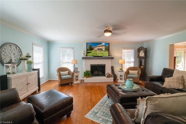 living room featuring a ceiling fan, wood finished floors, baseboards, crown molding, and a large fireplace