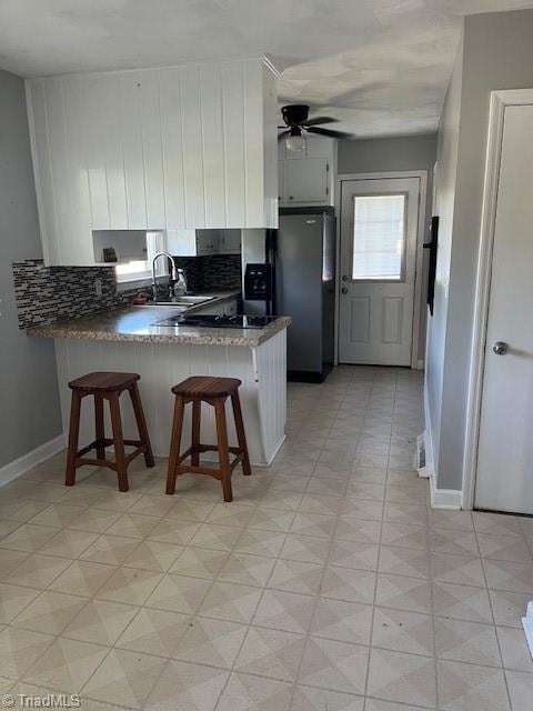 kitchen featuring white cabinetry, sink, stainless steel refrigerator with ice dispenser, kitchen peninsula, and a breakfast bar