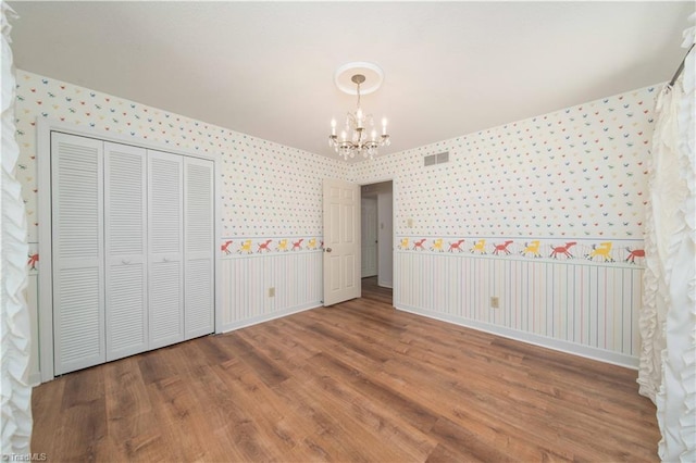 3306 Midkiff Rd, Winston-Salem, NC 27106 - unfurnished bedroom with wallpapered walls, a chandelier, wood finished floors, a closet, and baseboards