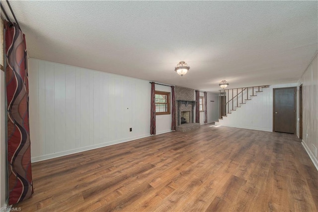 3306 Midkiff Rd, Winston-Salem, NC 27106 - unfurnished living room featuring wood finished floors, a brick fireplace, stairway, a textured ceiling, and baseboards