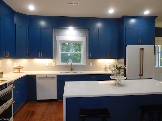 kitchen with white appliances, visible vents, a sink, a kitchen breakfast bar, and blue cabinets