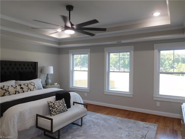 bedroom featuring baseboards, wood finished floors, a tray ceiling, and ornamental molding