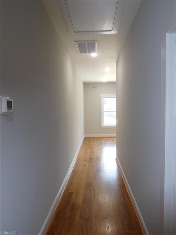 corridor with visible vents, attic access, baseboards, and wood finished floors