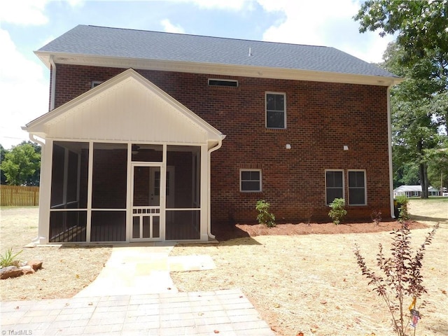 rear view of house with brick siding, a shingled roof, and a sunroom