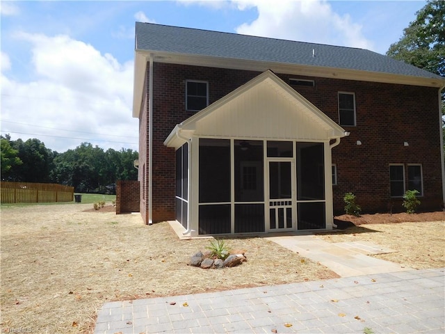 rear view of house with brick siding, fence, and a sunroom