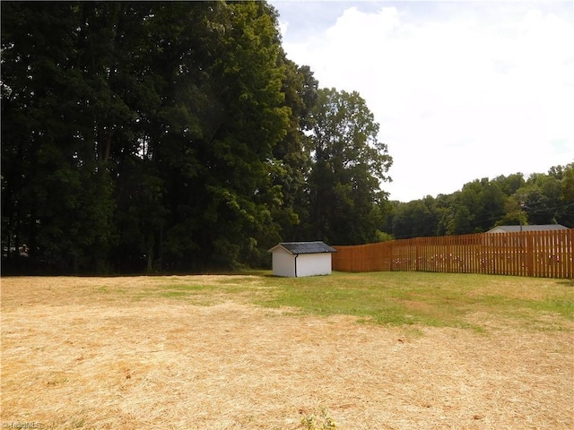 view of yard featuring a wooded view, an outdoor structure, a shed, and fence