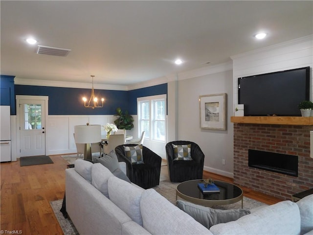 living room featuring visible vents, a notable chandelier, wood finished floors, crown molding, and a brick fireplace