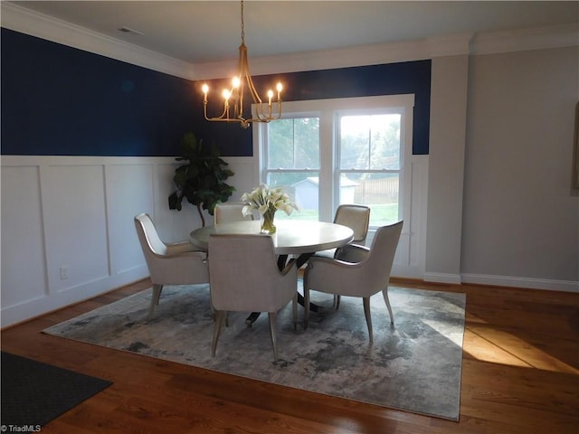 dining room featuring a wainscoted wall, visible vents, a notable chandelier, ornamental molding, and wood finished floors