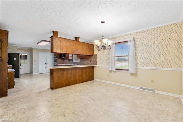 kitchen with kitchen peninsula, a textured ceiling, crown molding, pendant lighting, and stainless steel refrigerator