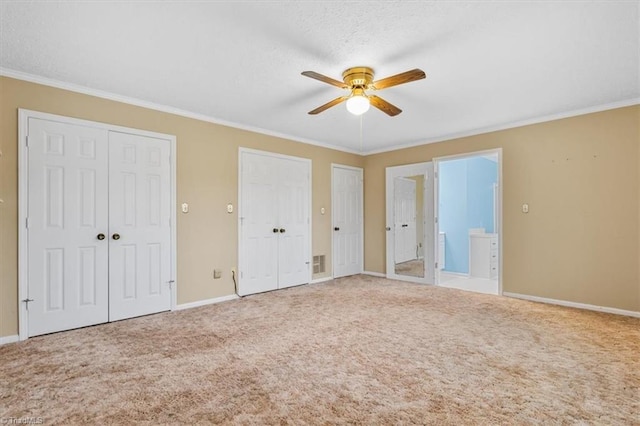 unfurnished bedroom featuring carpet, ceiling fan, ornamental molding, and multiple closets