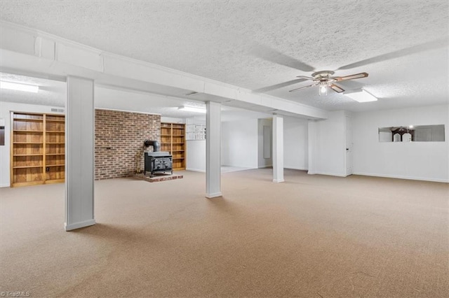 basement featuring a wood stove, ceiling fan, a textured ceiling, carpet floors, and brick wall