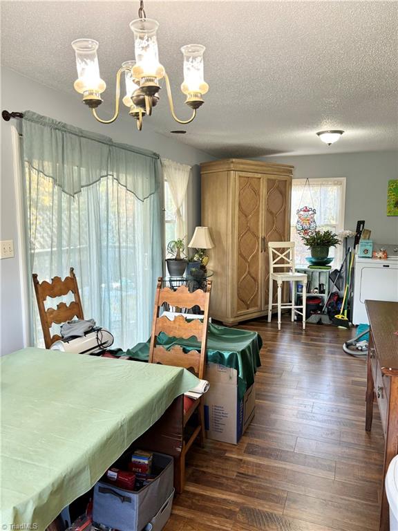 dining room featuring dark wood-type flooring, a chandelier, a textured ceiling, and washer / dryer