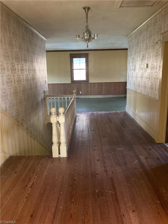 corridor featuring crown molding, dark wood-type flooring, and an inviting chandelier