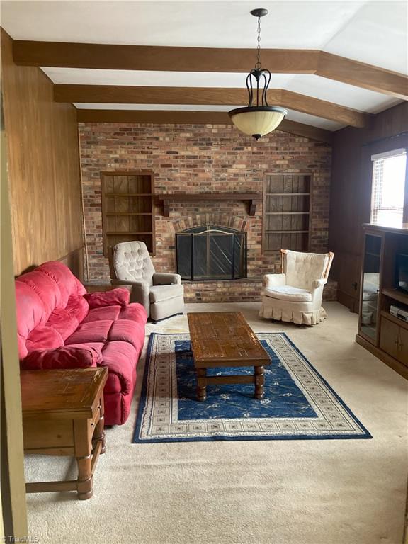 carpeted living room featuring vaulted ceiling with beams, a fireplace, and wood walls