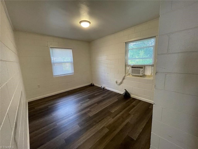 spare room with concrete block wall, cooling unit, dark wood-style floors, and a wealth of natural light