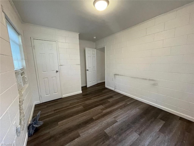 unfurnished bedroom featuring concrete block wall, baseboards, and dark wood-type flooring