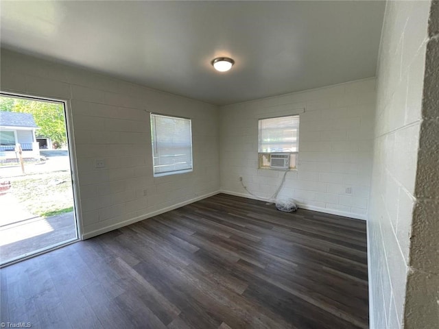 empty room featuring concrete block wall, cooling unit, dark wood-style floors, and a wealth of natural light