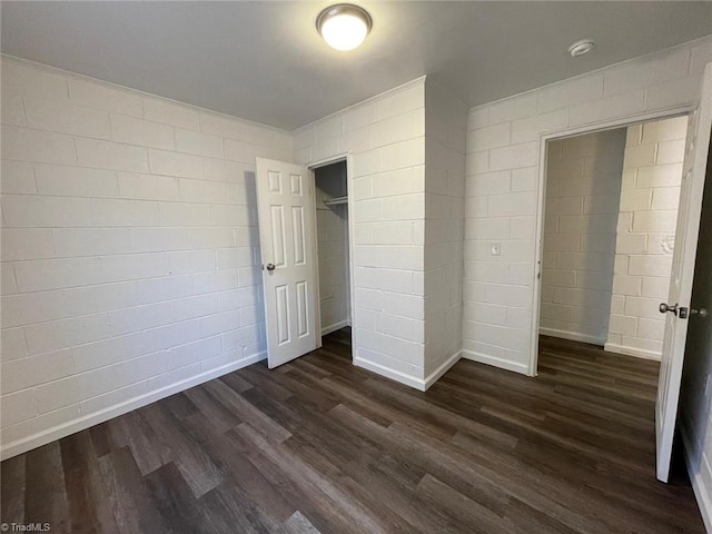 unfurnished bedroom with dark wood-style flooring, baseboards, and concrete block wall