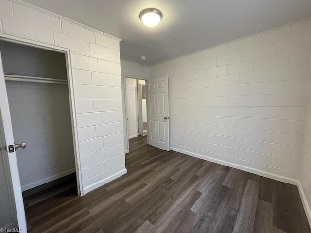unfurnished bedroom with a closet, dark wood finished floors, and concrete block wall