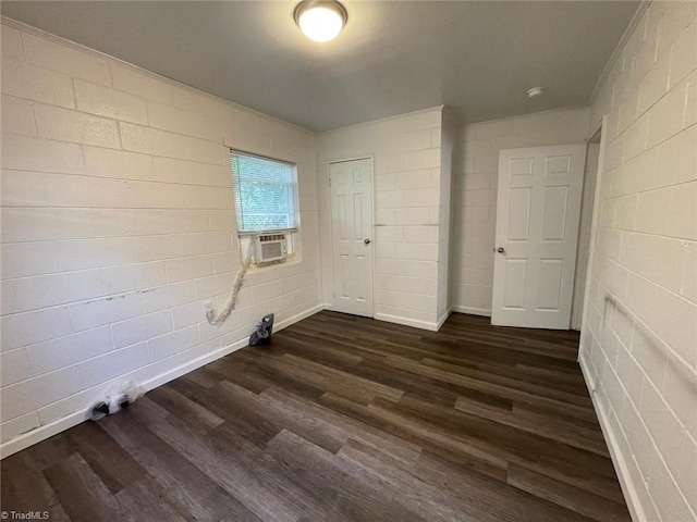 empty room featuring concrete block wall, dark wood finished floors, and cooling unit