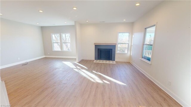 unfurnished living room featuring a tile fireplace, light wood-type flooring, and a healthy amount of sunlight